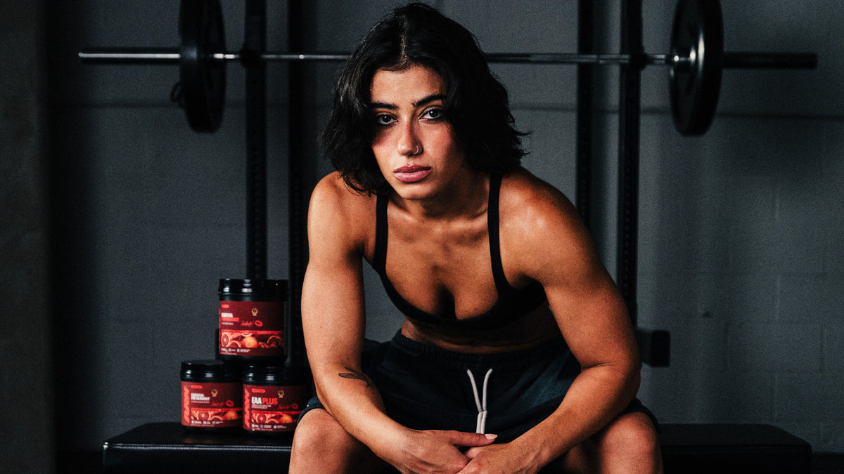 Sara Saffari seated on a gym bench beside RAW Sour Blood Orange Essential Pre-Workout, Essential Performance and EAA Plus