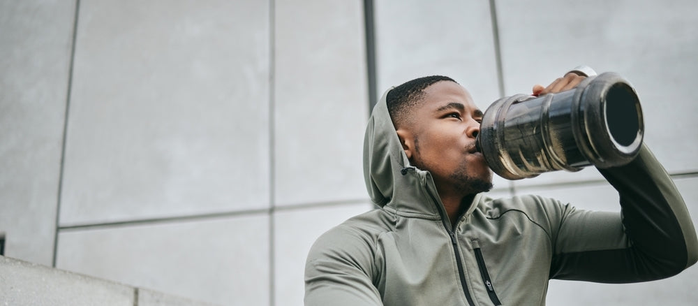 black man sitting down wearing a hoodie. Drinking a large bottle of water.