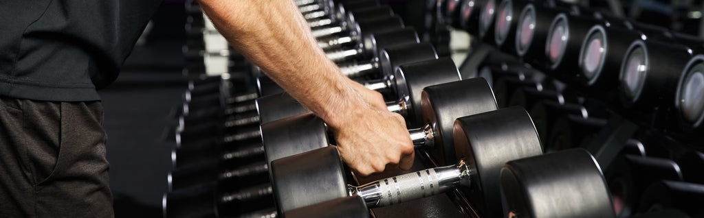 man at gym picking up dumbbell 