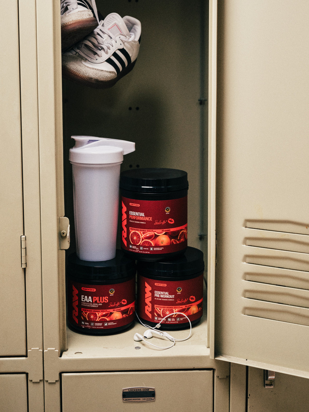 Sara Saffari Sour Blood Orange EAA Plus, Essential Performance and Essential Pre-Workout with a shaker and sneakers in a gym locker