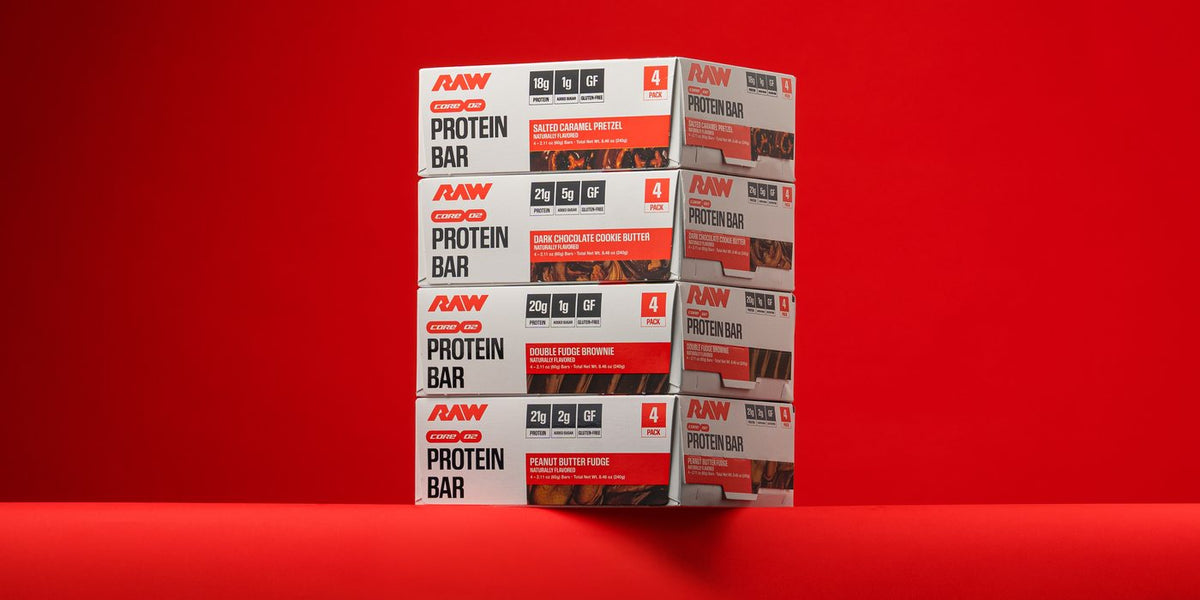 Stack of four RAW Core Protein Bar 4-pack boxes in Salted Caramel Pretzel, Dark Chocolate Cookie Butter, Double Fudge Brownie and Peanut Butter Fudge on a red background.