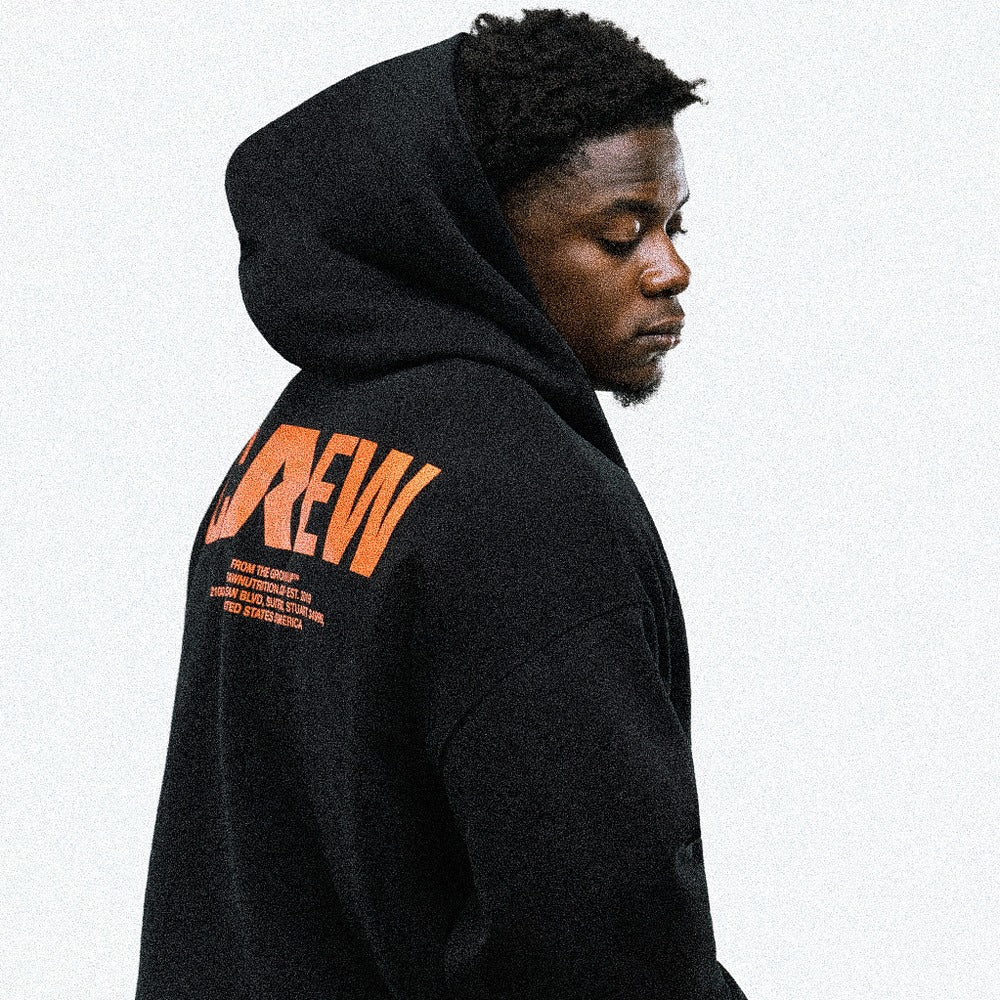 Athlete in the black RAW Core Crew Hoodie, hood up, looking over his shoulder to show the orange CREW back graphic