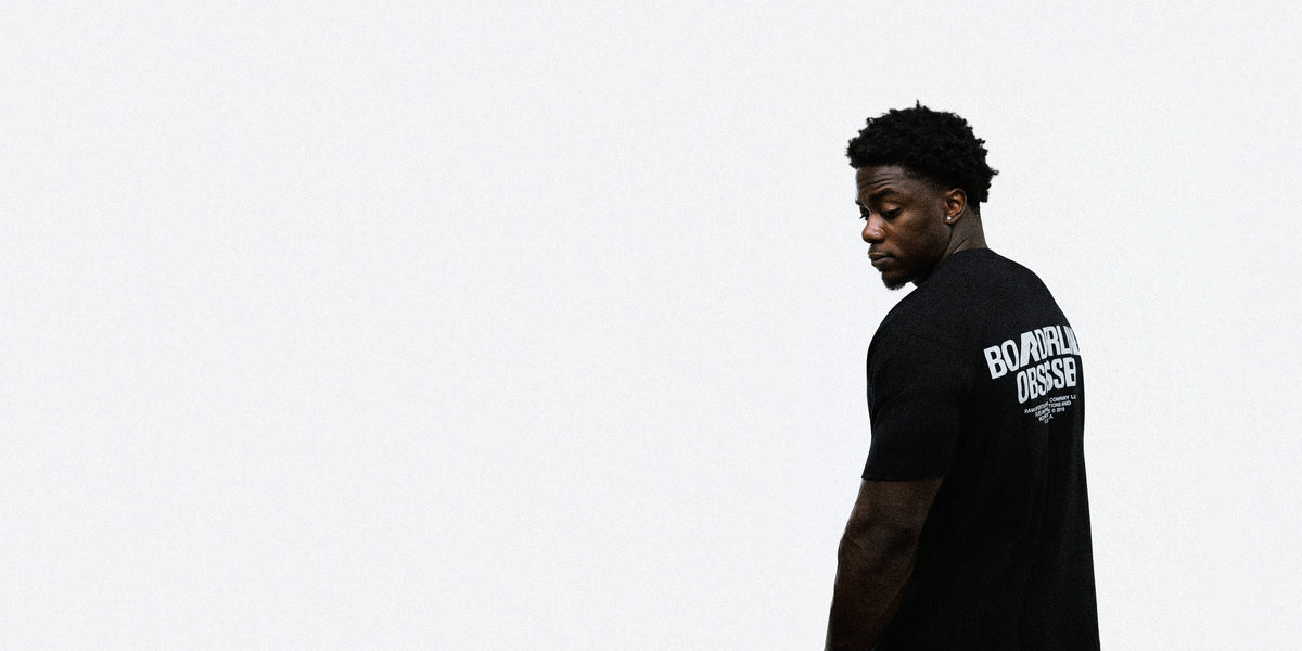 Athlete looking over his shoulder in the black RAW Core Borderline Obsessed T-Shirt, back graphic in light grey, against a light grey studio background